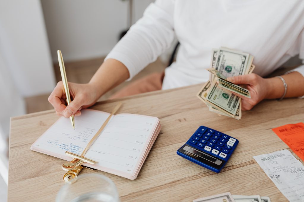 woman holding cash sitting at a table with a calculator and notebook doing budgeting